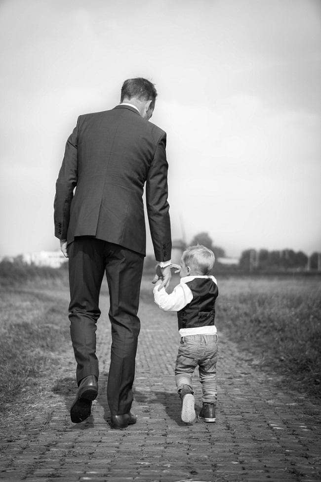 A father holding his sons hand walking off together with backs turned to camera